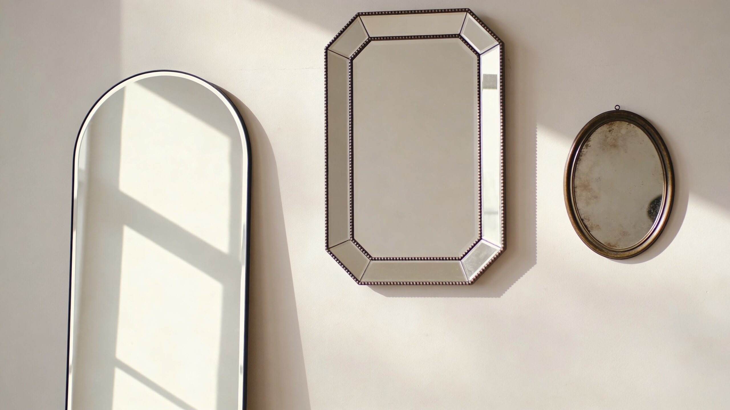 Three different decorative mirrors in arch, rectangular, and oval shapes hanging on a plain white wall.
