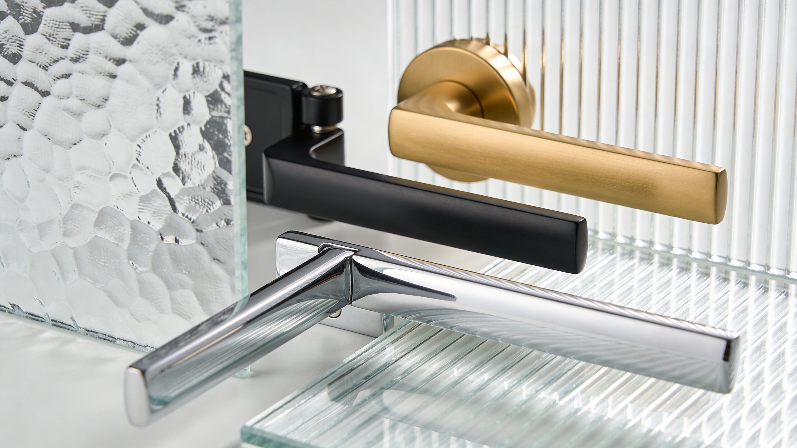 Three different modern door handle designs in gold, matte black, and chrome finishes against glass surfaces.