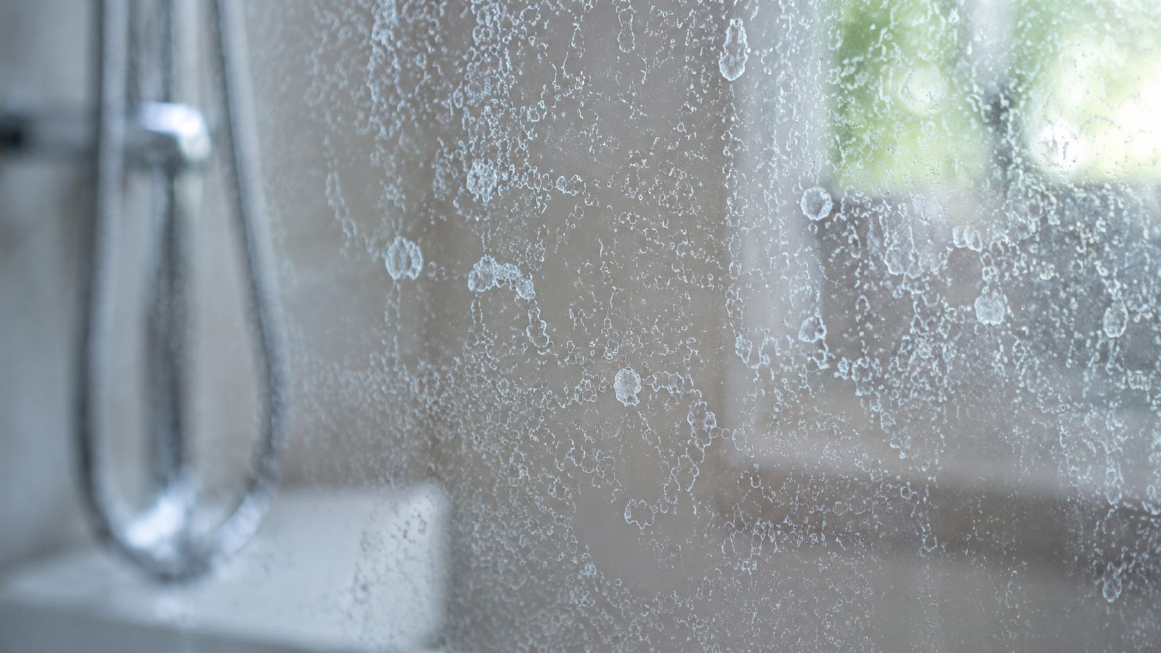 Close up view of persistent white mineral water spots covering a transparent shower glass screen.