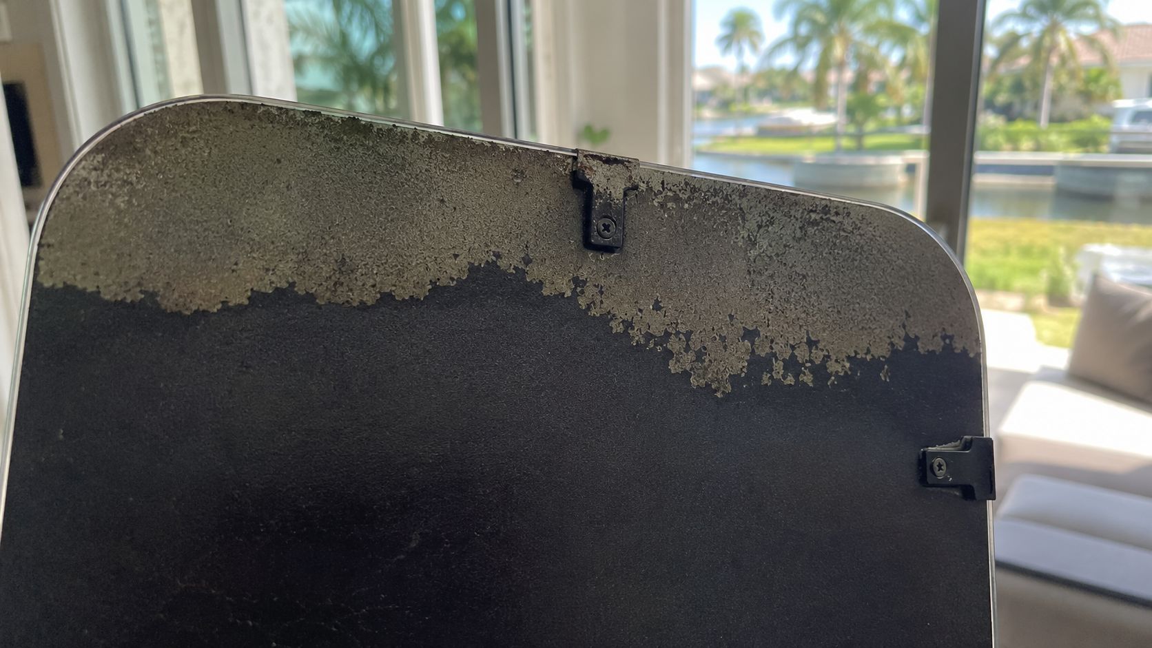 A close-up view showing the damaged silver backing of a frameless wall mirror and its mounting hardware.